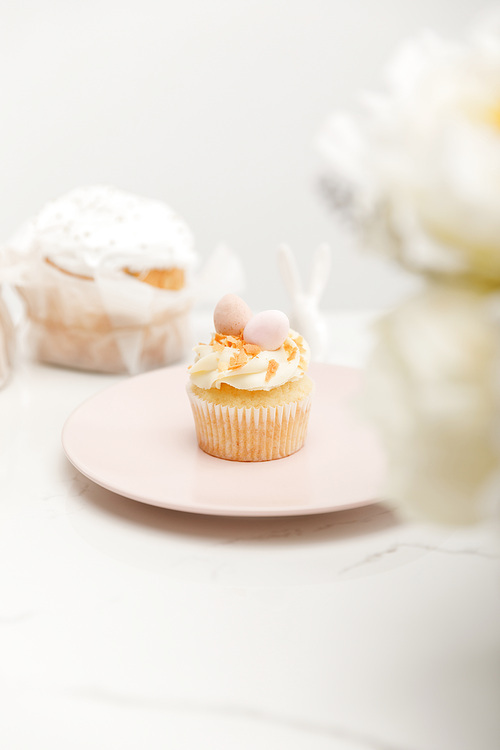 Selective focus of cupcake on plate and flowers on white background