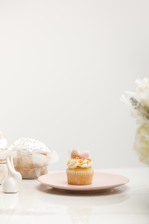 selective focus of cupcake on plate, . cake, decorative rabbit and flowers isolated on grey