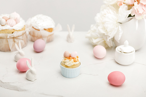selective focus of cupcake with colorful chicken eggs, decorative bunnies, sugar bowl, . cakes and flowers isolated on grey