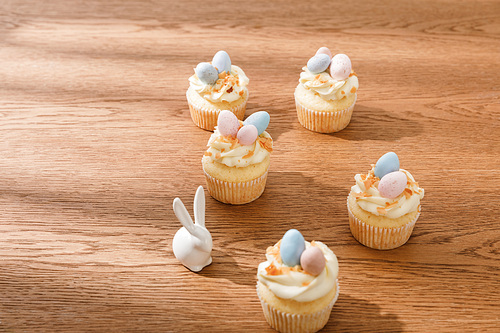 Delicious cupcakes with decorative bunny on wooden background