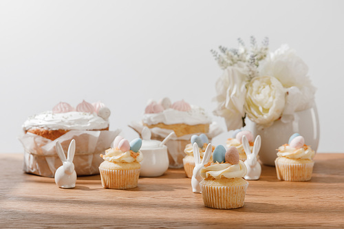 selective focus of cupcakes with decorative bunnies, sugar bowl, . cakes and vase with flowers isolated on grey