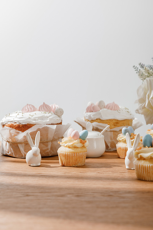 Selective focus of cupcakes with decorative bunnies, sugar bowl, easter cakes and flowers isolated on grey