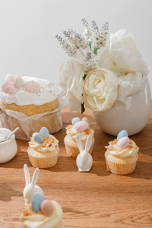 selective focus of cupcakes with decorative bunnies, sugar bowl, . bread and vase isolated on grey
