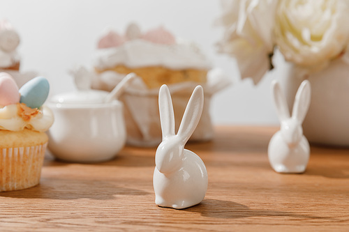 Selective focus of decorative bunnies, cupcake, sugar bowl, and flowers on wooden background