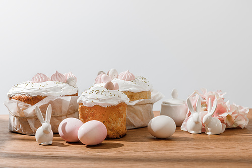 Decorative bunnies, chicken eggs, sugar bowl, Easter cakes and petals isolated on grey