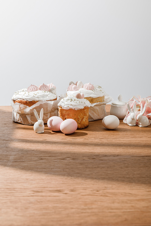 Decorative bunnies, petals, chicken eggs and sugar bowl near Easter cakes isolated on grey