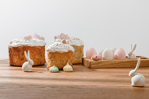 Decorative bunnies, chicken and quail eggs on egg tray, meringues near Easter cakes isolated on grey