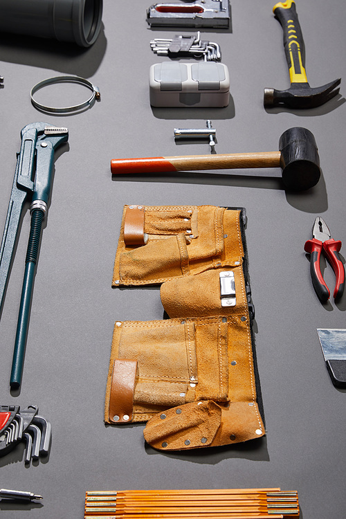 high angle view of tool belt, hammers, monkey wrench, putty knife, pliers, calipers, rivet gun, angle keys and stapler on grey background