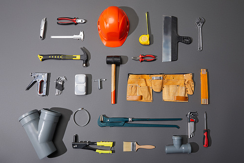 flat lay of industrial tools, helmet, measuring tape, tool belt and brush on grey background