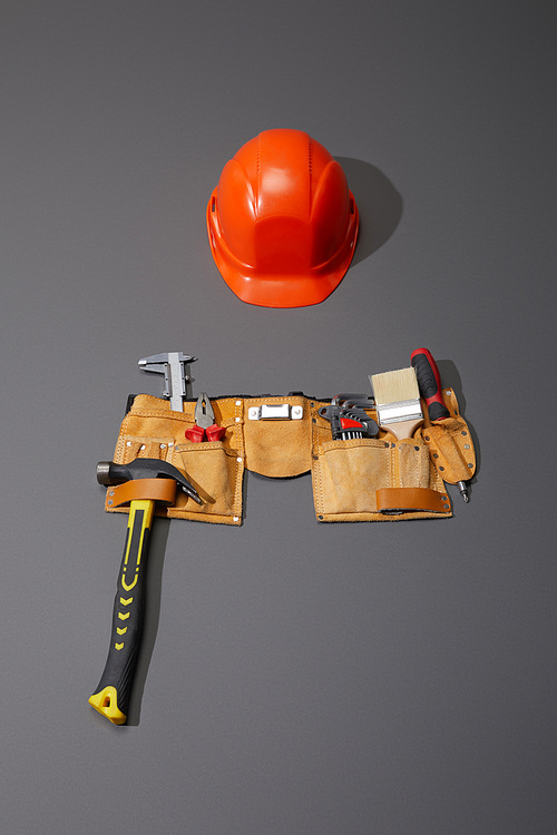 high angle view of helmet, tool belt with hammer, brush, pliers, calipers, angle keys and screwdriver on grey background