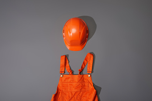 top view of orange helmet and overalls on grey background