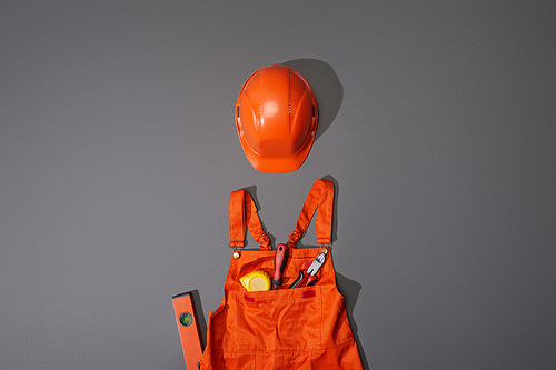 top view of orange helmet and overalls with measuring tape, screwdriver and pliers on grey background