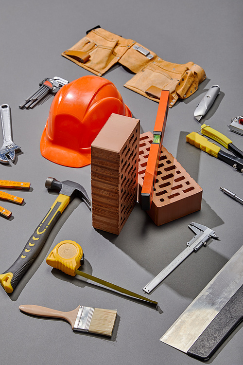 high angle view of bricks, industrial tools and helmet on grey background