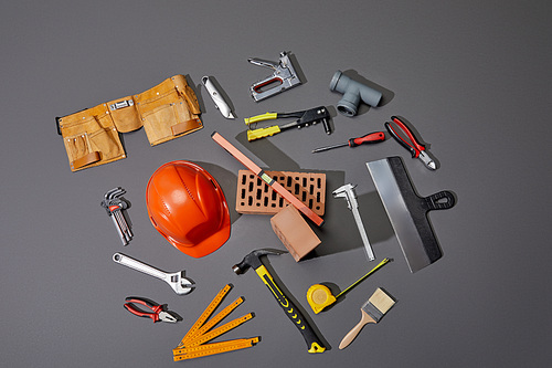 top view of bricks, tool belt, helmet and industrial tools on grey background