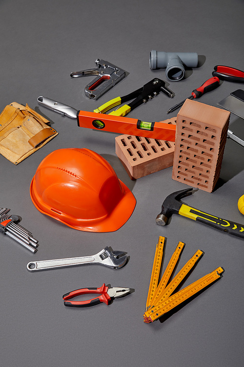 high angle view of tool belt, bricks, industrial tools and orange helmet on grey background