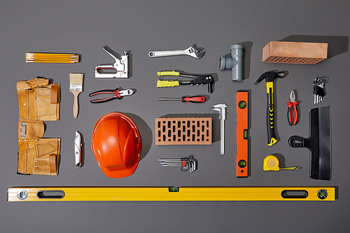 flat lay with bricks, orange helmet, tool belt and industrial tools on grey background