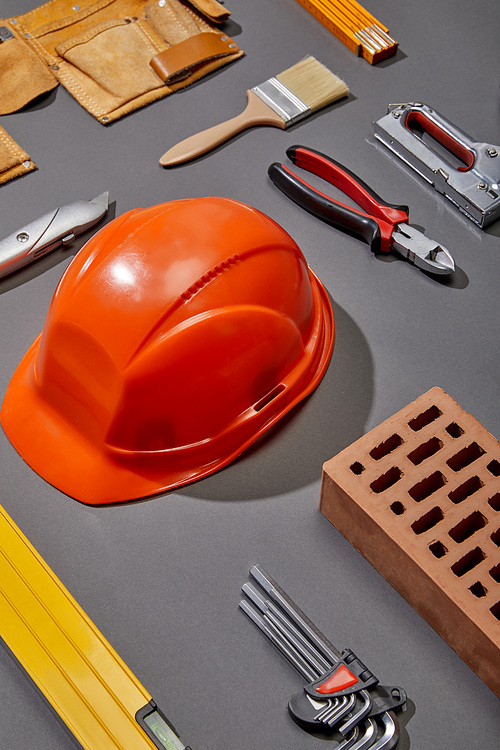 flat lay with orange helmet, brick, brush, brick, tool belt and industrial tools on grey background