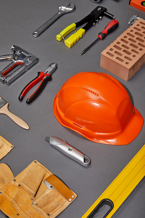 flat lay with orange helmet, tool belt, brick, industrial tools and brush on grey background