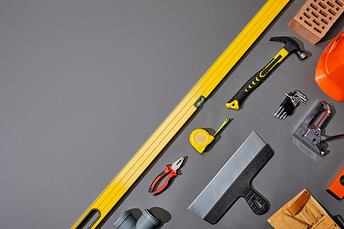 flat lay with brick, hammer, measuring tape, helmet, tool belt and industrial tools on grey background