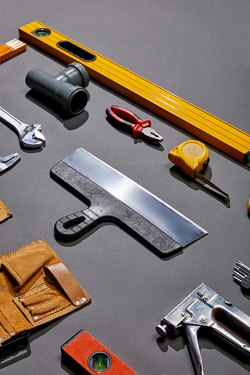 high angle view of putty knife, spirit levels, pipe connector, pliers, measuring tape, monkey wrench, tool belt and stapler on grey background