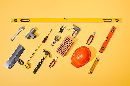 flat lay with industrial tools, brick and orange helmet on yellow background