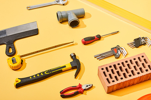 flat lay with hammer, pipe connector, angle keys, screwdriver, pliers, brick, measuring tape and putty knife on yellow background