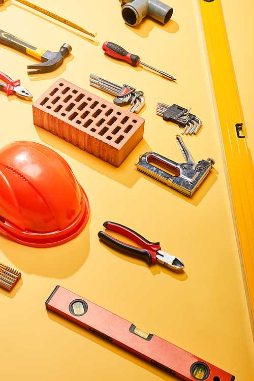 flat lay with industrial tools, brick and helmet on yellow background