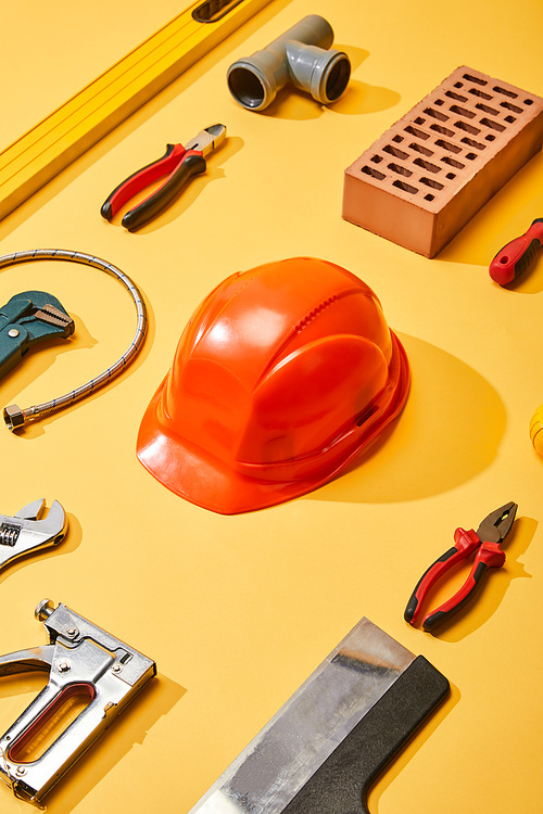 flat lay with industrial tools, helmet and brick, on yellow background