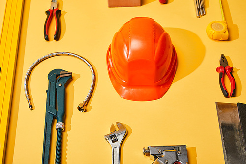 flat lay with helmet, calipers, monkey wrench, putty knife, plumbing hose, spirit level, measuring tape and angle keys on yellow background