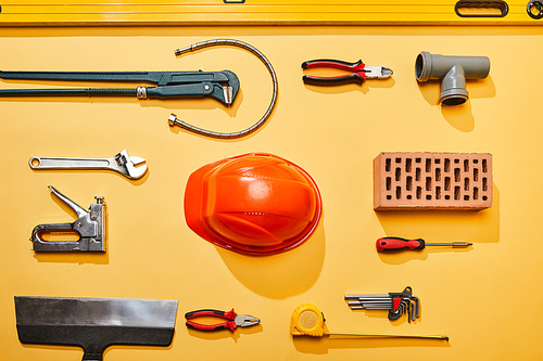 top view of industrial tools, helmet, plumbing hose and brick on yellow background