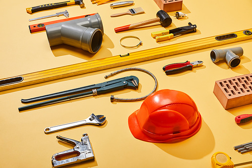 high angle view of industrial tools, helmet, bricks, measuring tape, brush, and plumbing hose on yellow background