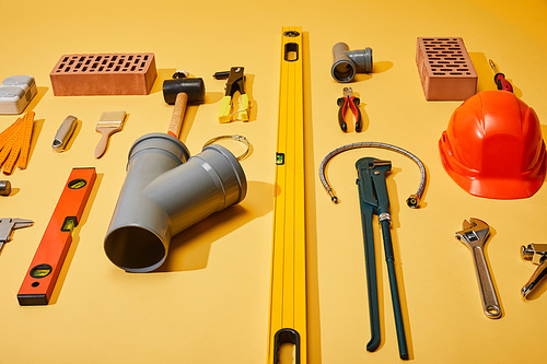 high angle view of industrial tools, bricks and helmet on yellow background