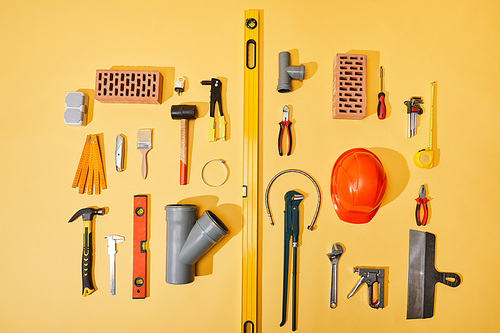 top view of bricks, industrial tools, helmet, plumbing hose, and measuring tape on yellow background