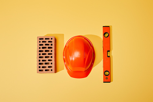 top view of brick, orange helmet and spirit level on yellow background