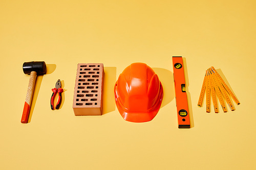 flat lay with hammer, pliers, brick, helmet, spirit level and folding ruler on yellow background