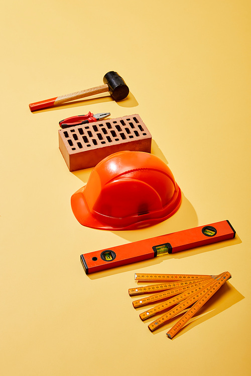 high angle view of hammer, pliers, brick, helmet, spirit level and folding ruler on yellow background