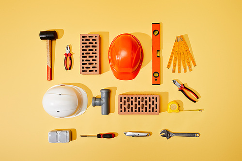 top view of bricks, helmets, measuring tape, and industrial tools on yellow background