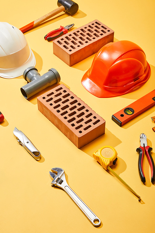 high angle view of bricks, helmets, and industrial tools on yellow background