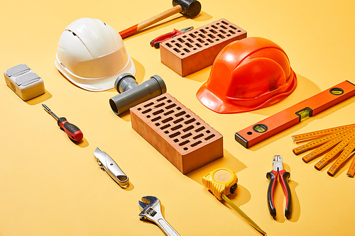 high angle view of industrial tools, bricks and helmets on yellow background