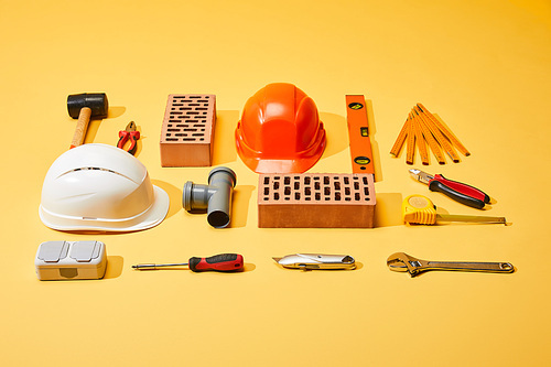 flat lay with bricks, helmets, industrial tools and measuring tape on yellow background