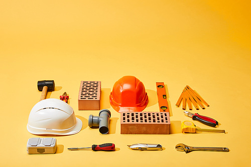 high angle view of bricks, helmets, and industrial tools on yellow background