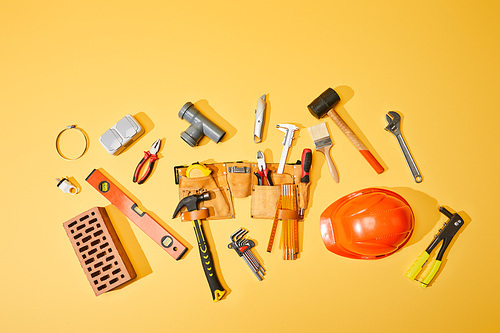 top view of tool belt, brick, industrial tools and helmet on yellow background