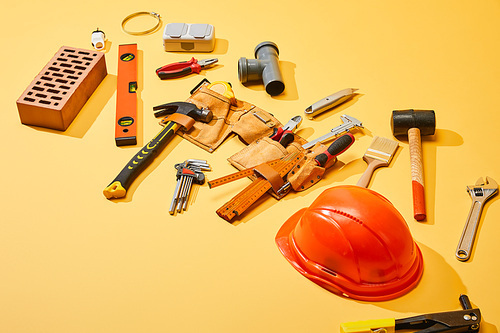 high angle view of tool belt with industrial tools, brick and helmet on yellow background