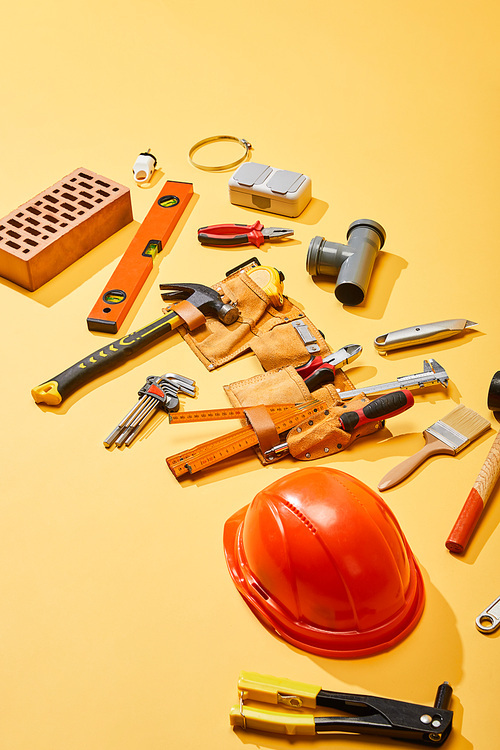 high angle view of tool belt, industrial tools, brick and helmet on yellow background