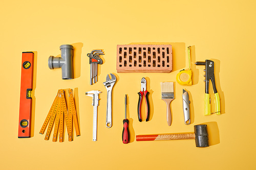 top view of industrial tools and brick on yellow background