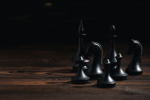 chess figures on wooden surface isolated on black