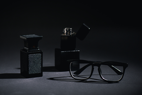 selective focus of glasses and perfume bottle near lighter on black