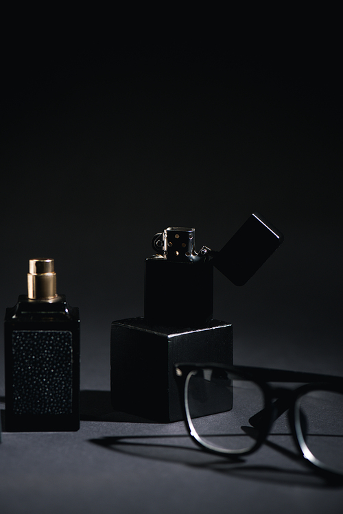 selective focus of lighter near glasses and perfume bottle on black