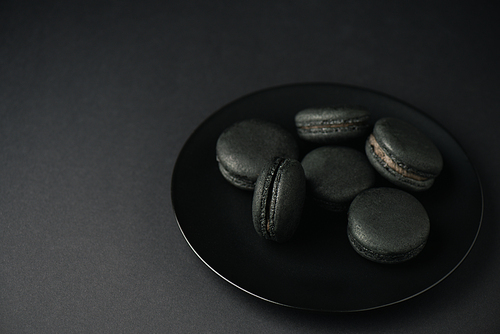 plate with tasty and dark macarons isolated on black