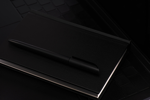 close up of black notebook and pen on laptop keyboard